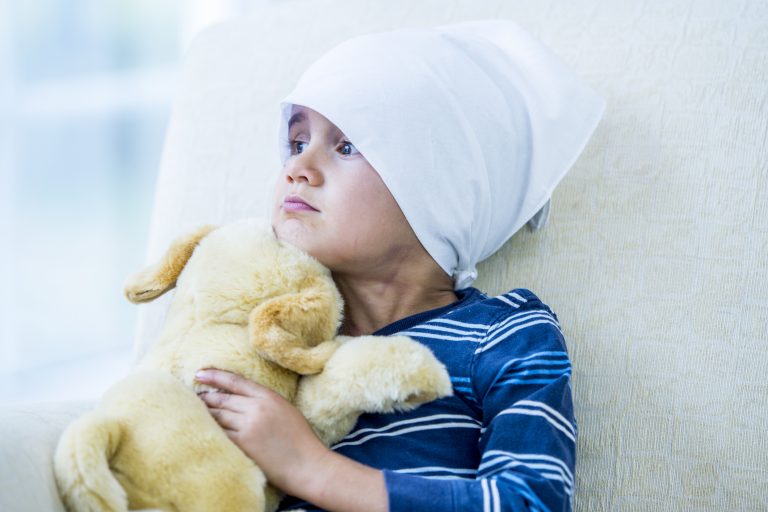Young, male, brain cancer patient wearing a hat/head covering is sitting in bed With a Toy Dog. Image signifies use of precision cancer therapy to improve outcomes.