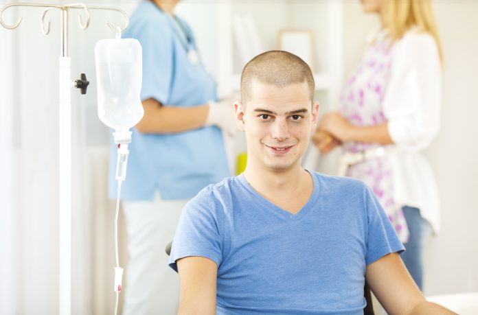 Photo of an young antheral   receiving chemotherapy astatine  home. In inheritance  his woman  talking with nurse. Illustrating crab  epigenetics.