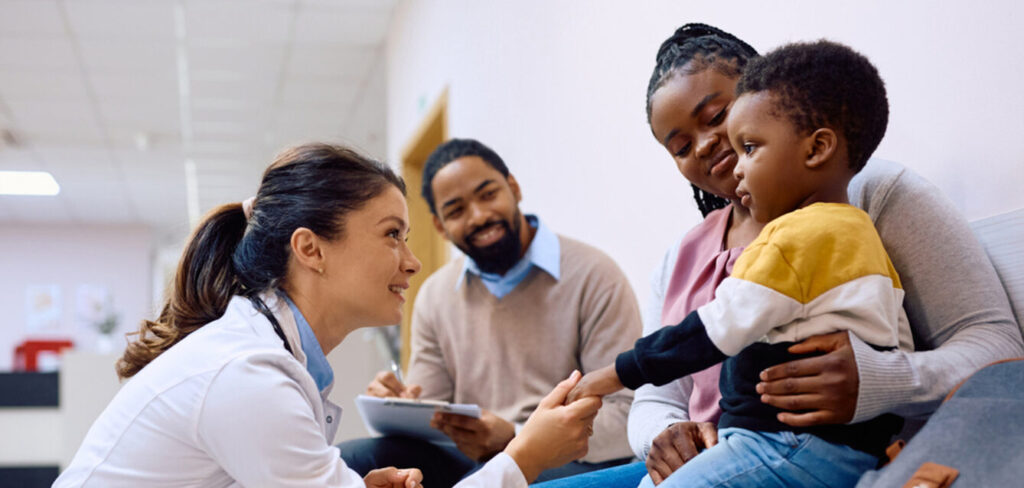 Female pediatrician talking to black little boy who is sitting on mother's lap at the clinic.