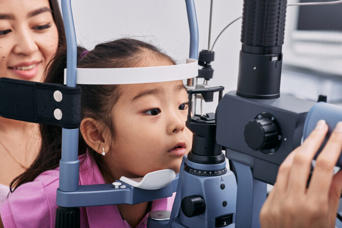 Image of a small Asian girl having her eyes photographed by an ophthalmologist, with an Asian women sitting behind her to check for myopia or near-sightedness