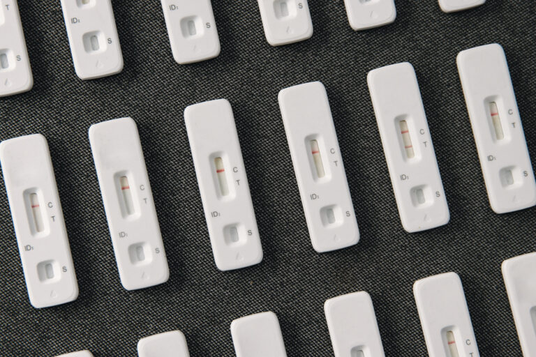 Abstract photo of rows of used Lateral Flow Tests - one showing a positive result