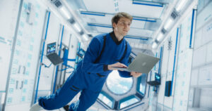 Caucasian Male Astronaut Using Laptop to Wirelessly Connect to a Satellite. Scientist Working on Computer Device Inside an Intergalactic Station. Professional Engineer Undertaking Online Service Job